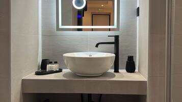 A modern bathroom with a large mirror, a round vanity mirror, a white sink, and a towel rack.