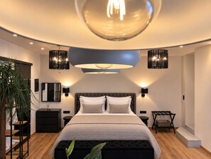 A modern bedroom with a large bed, bedside lamps, a hanging light fixture, and a plant. - Apollonio Suites (Corinth)