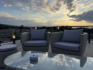 A wicker sofa with cushions, a glass table with a candle, and a railing overlooking a scenic view. - Apollonio Suites (Corinth)