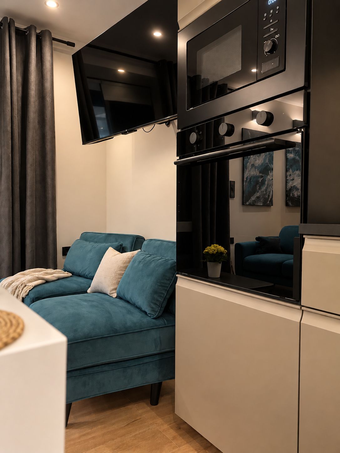 Un espacio de estar moderno con un sofá, un televisor de pantalla plana montado en la pared y un microondas sobre una zona de cocina.