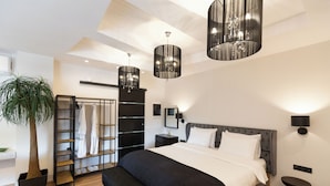 A modern bedroom with a large bed, a bench, a plant, a wardrobe, and pendant lights. - Apollonio Suites (Corinth)