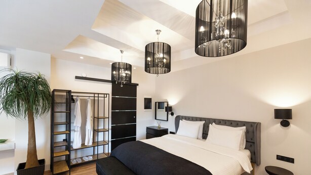 Une chambre à coucher moderne avec un grand lit, un banc, une plante, une armoire et des lampes suspendues.