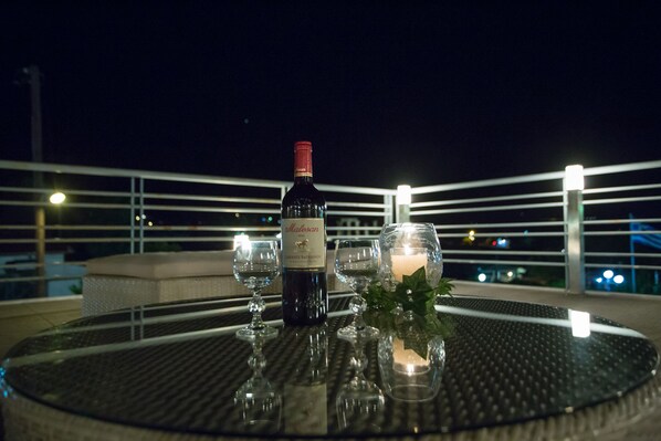 A table with a bottle of wine, two glasses, and a candle on a balcony at night.