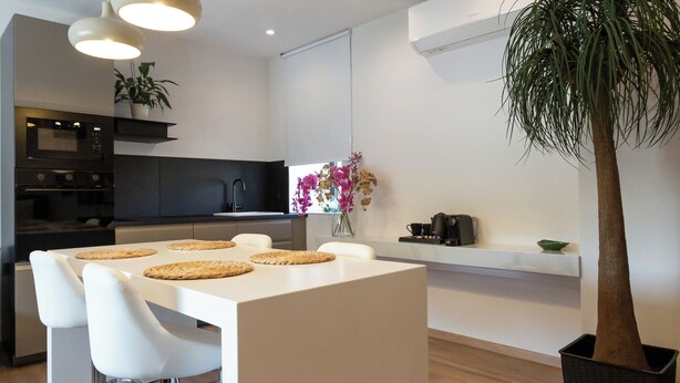 A modern kitchen with a central island, pendant lights, and a potted plant. - Apollonio Suites (Corinth)