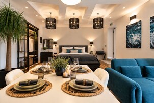 A modern hotel room with a large bed, a dining area set for two, and a blue sofa.
