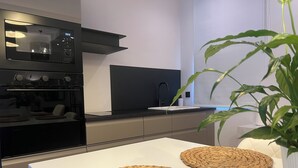 A modern kitchen with a built-in oven, a black range hood, and a white countertop. - Apollonio Suites (Corinth)