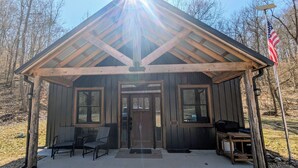 A rustic cabin with a gabled roof, two windows, a front door, and a small porch with two chairs.