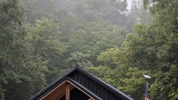 A cabin with a gabled roof, a front porch, and an American flag.