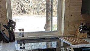 A kitchen with a stainless steel stove, wooden cabinets, and a window with a view of trees.