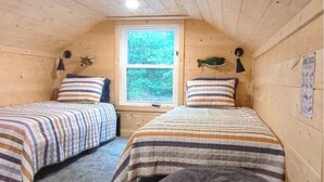 A cozy cabin bedroom with two beds, a window, and a large bean bag chair.