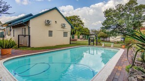 Une piscine bordée de briques, un bâtiment équipé de climatiseurs et un jardin clos.