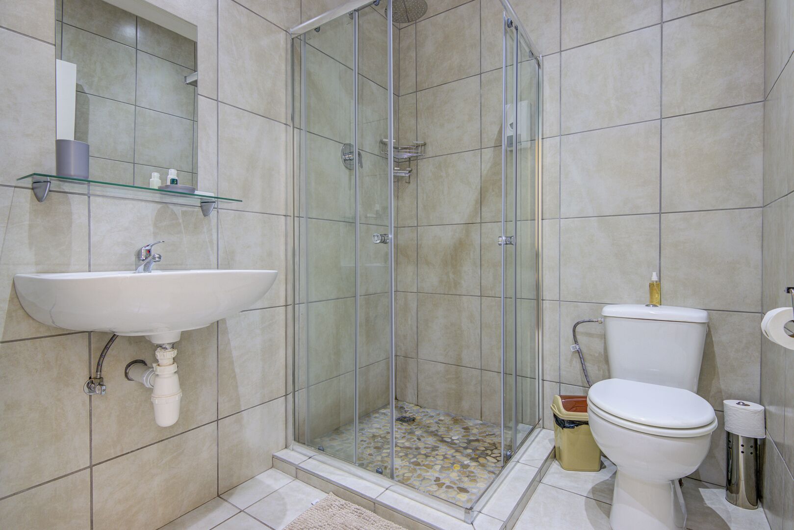 A bathroom with a glass-enclosed shower, a sink with a mirror above it, and a toilet with a paper towel dispenser.