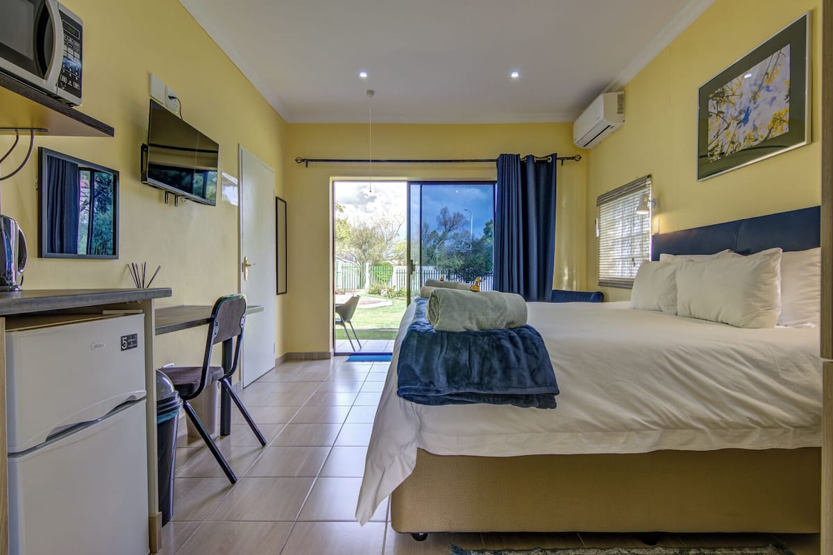 Een hotelkamer met een bed, een bureau met een computer, een stoel, een kleine kitchenette en een schuifdeur naar een balkon.