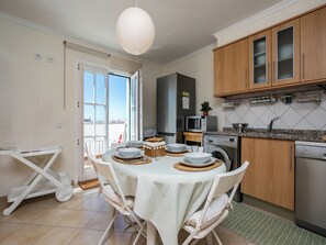Cozinha moderna com área de jantar, incluindo uma mesa posta para quatro pessoas, micro-ondas, máquina de lavar e armários de madeira.