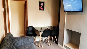 Ein Wohnzimmer mit grauem Sofa, einem kleinen Tisch mit Stühlen, einem flachbildfernseher an der Wand und einem gerahmten Bild von einem Flamingo.