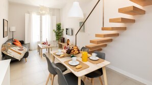 A modern living space with a dining area, a staircase, and a sofa. - Luxury Suite Tico San Diego (Granada)