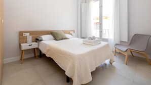 A modern bedroom with a bed, bedside table, chair, and a view of the outside. - Luxury Suite Tico San Diego (Granada)