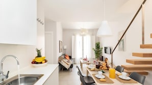 A modern kitchen with a sink, dining table, chairs, and a staircase. - Luxury Suite Tico San Diego (Granada)