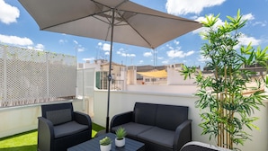 A rooftop patio with wicker furniture, a table, and a large umbrella. - Luxury Suite Tico San Diego (Granada)