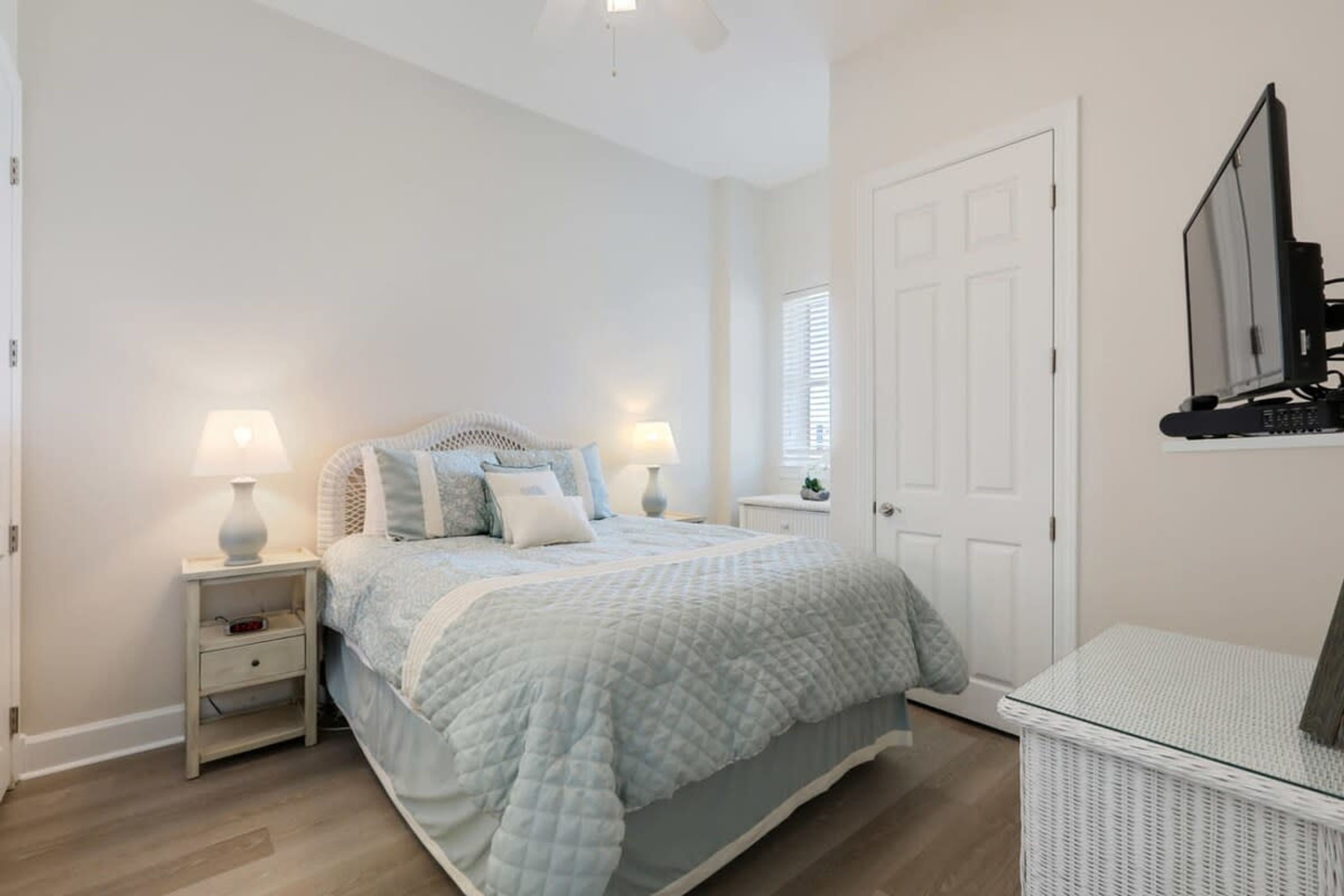 A bedroom with a bed, nightstands, a lamp, a TV, and a wicker basket.