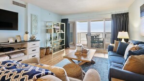 A modern living room with a sofa, coffee table, and a TV. There is a balcony with a view. - Sandy Key 635 2 BD 2BH 6th Floor (Pensacola)
