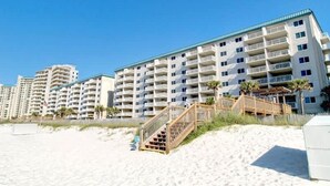 A beachfront hotel with multiple balconies, a sandy beach in front, and a wooden staircase leading to the entrance. - Sandy Key 635 2 BD 2BH 6th Floor (Pensacola)