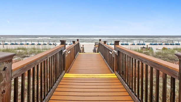 A wooden boardwalk leading to a beach with rows of beach chairs and umbrellas. - Sandy Key 635 2 BD 2BH 6th Floor (Pensacola)