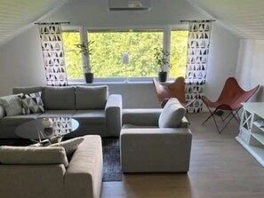 A modern living room with a sectional sofa, a small table, and two chairs. There are potted plants and a view of greenery outside. - 5 Star Holiday Home in Mollosund (Mollösund)