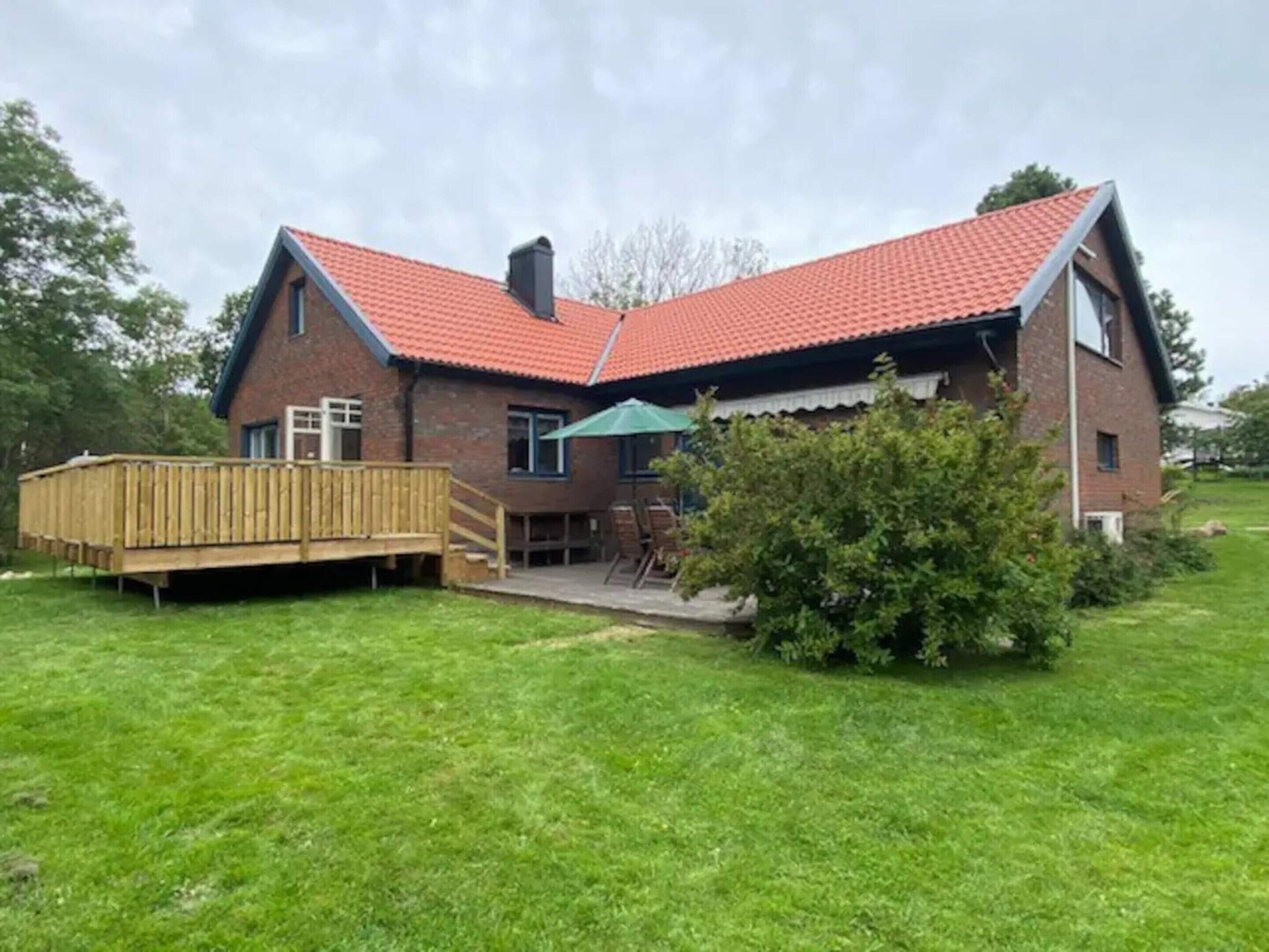 A two-story brick house with a red-tiled roof, a wooden deck, and a small patio area.
