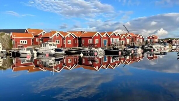 A row of red houses with a calm body of water reflecting them. - 5 Star Holiday Home in Mollosund (Mollösund)