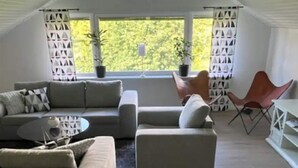 A modern living room with a sectional sofa, a small coffee table, and a red chair. There are two potted plants and a window with curtains. - 5 Star Holiday Home in Mollosund (Mollösund)