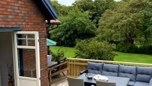 An outdoor patio with a wooden deck, a built-in seating area with cushions, and a view of a green garden. - 5 Star Holiday Home in Mollosund (Mollösund)