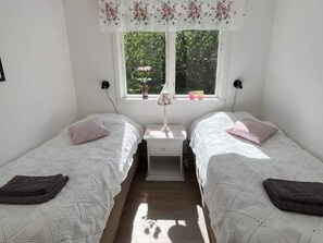 A bedroom with two single beds, a nightstand with a lamp, and a window with a view of greenery. - 5 Star Holiday Home in Mollosund (Mollösund)