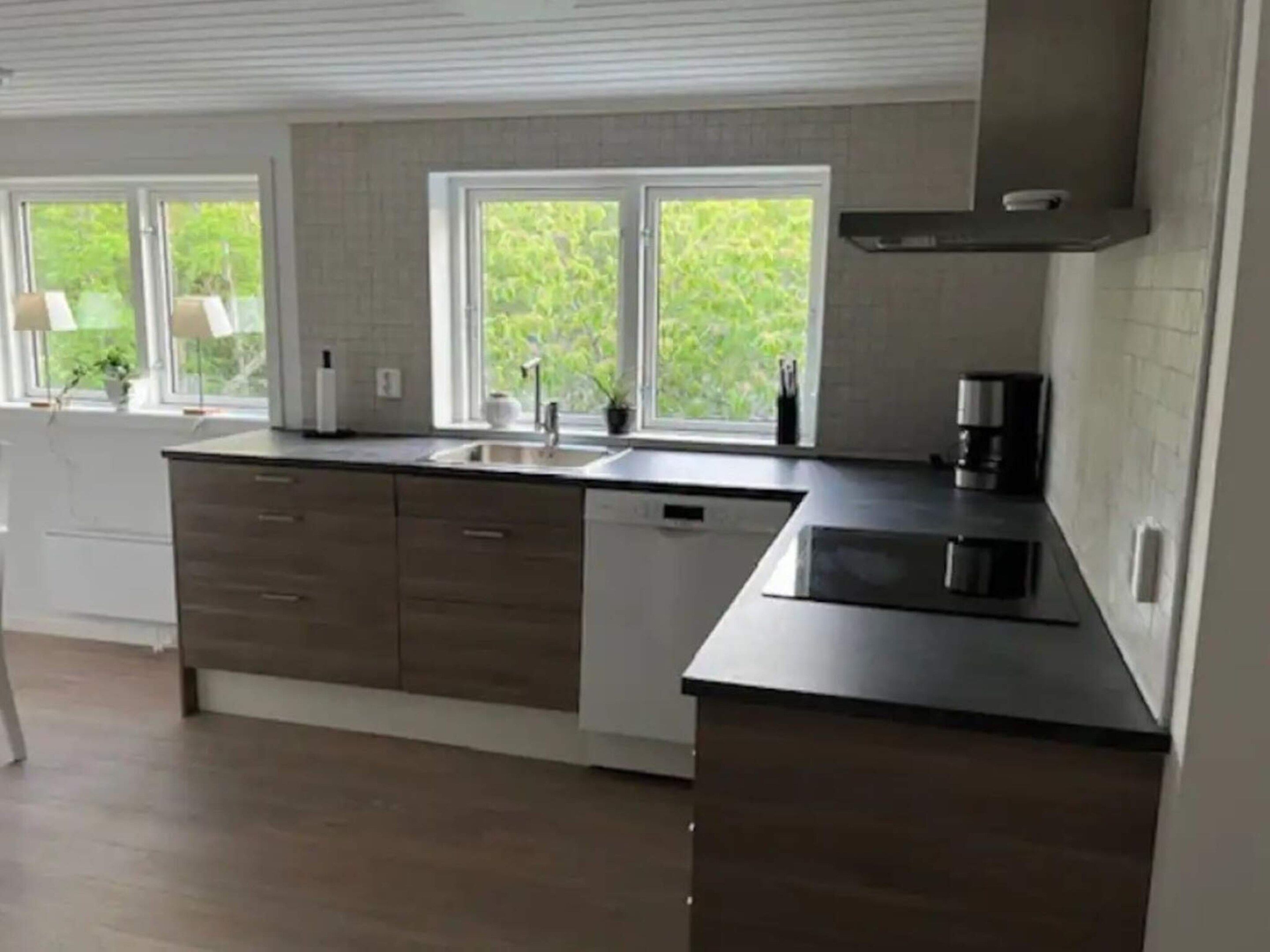 A modern kitchen with a large island, built-in appliances, and a view of greenery outside.