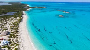 An aerial view of a coastal area with clear turquoise waters, sandy beaches, and sparse vegetation. - La Dolce Vita Cottage, Beachfront w/ pool directly on Tropic of Cancer Beach! (Moore Hill)