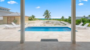 A pool area with a view of the beach, palm trees, and a clear sky. - La Dolce Vita Cottage, Beachfront w/ pool directly on Tropic of Cancer Beach! (Moore Hill)