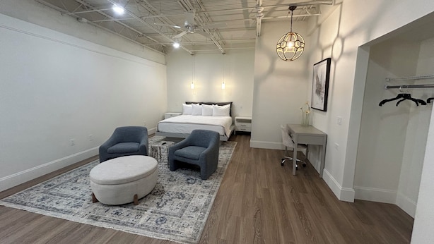 Un dormitorio moderno con una cama grande, dos sillones, una mesita y una lámpara colgante.