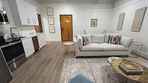 Un apartamento moderno con kitchenette, un sofá gris, una mesa de centro redonda y una puerta de madera.