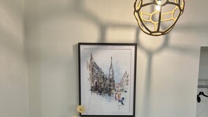 Una habitación con escritorio, silla y un cuadro enmarco de un paisaje urbano.