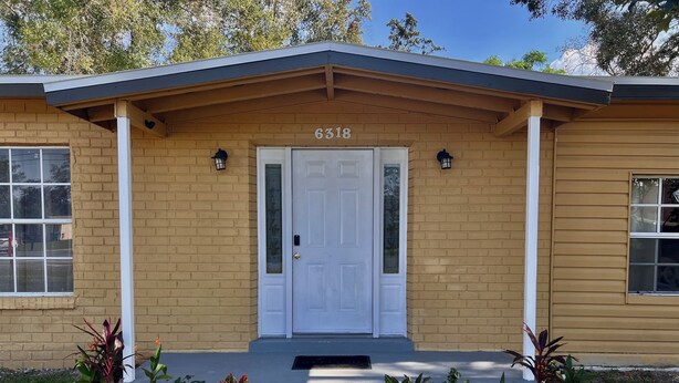 A two-story building with a beige exterior, a white front door, and a small porch with two potted plants. - Adventure Coast 4/2, Big Yard (Spring Hill)
