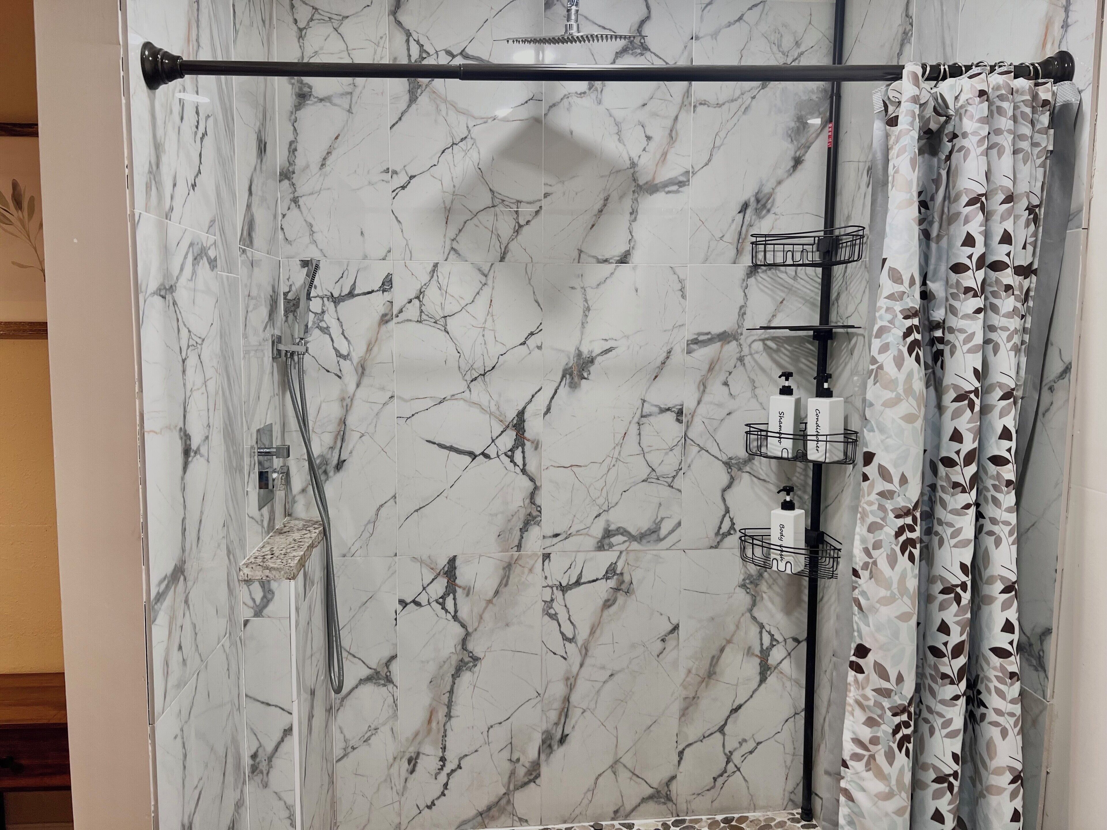 A bathroom with a marble shower wall, a towel rack, and a shower curtain with a leaf pattern.