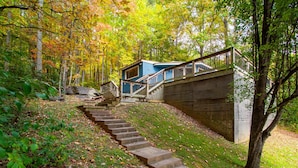 Eine Treppe führt zu einer blauen Hütte in einem bewaldeten Gebiet, versehen mit einem Metallgeländer.