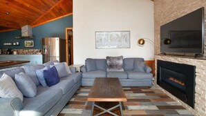 Ein Wohnzimmer mit grauem Sofa, einem Holztisch, einem Kamin und einem Fernseher.