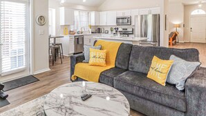 A modern living room with a gray sofa, yellow throw pillows, and a marble coffee table. - Upscale Home w/ Pool, Arcade & More! (Frisco)
