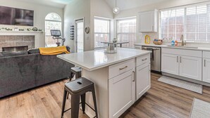 A modern kitchen with a central island, white cabinetry, and a built-in oven. - Upscale Home w/ Pool, Arcade & More! (Frisco)
