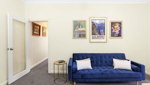 Une pièce avec un canapé en velours bleu, une petite table ronde et trois affiches encadrées accrochées au mur.