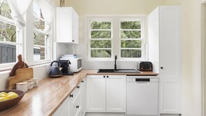 Une cuisine avec des meubles blancs, un plan de travail en bois, une bouilloire, un grille-pain et une fenêtre donnant sur un paysage verdoyant.