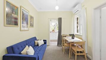 A room with a blue sofa, a wooden dining table with chairs, and framed pictures on the wall.