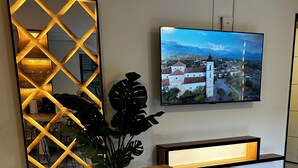 A modern dining area with a wooden table, a decorative wall panel, a large flat-screen TV, and a potted plant. - Beautiful 2-bedroom apartment in Medellín with Free WiFi, AC- Near El Poblado (Medellín)
