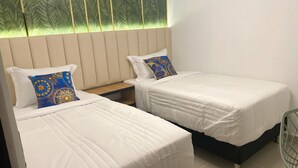 Two single beds with white linens and blue patterned pillows, a wooden nightstand, and a window with a palm leaf pattern. - Beautiful 2-bedroom apartment in Medellín with Free WiFi, AC- Near El Poblado (Medellín)